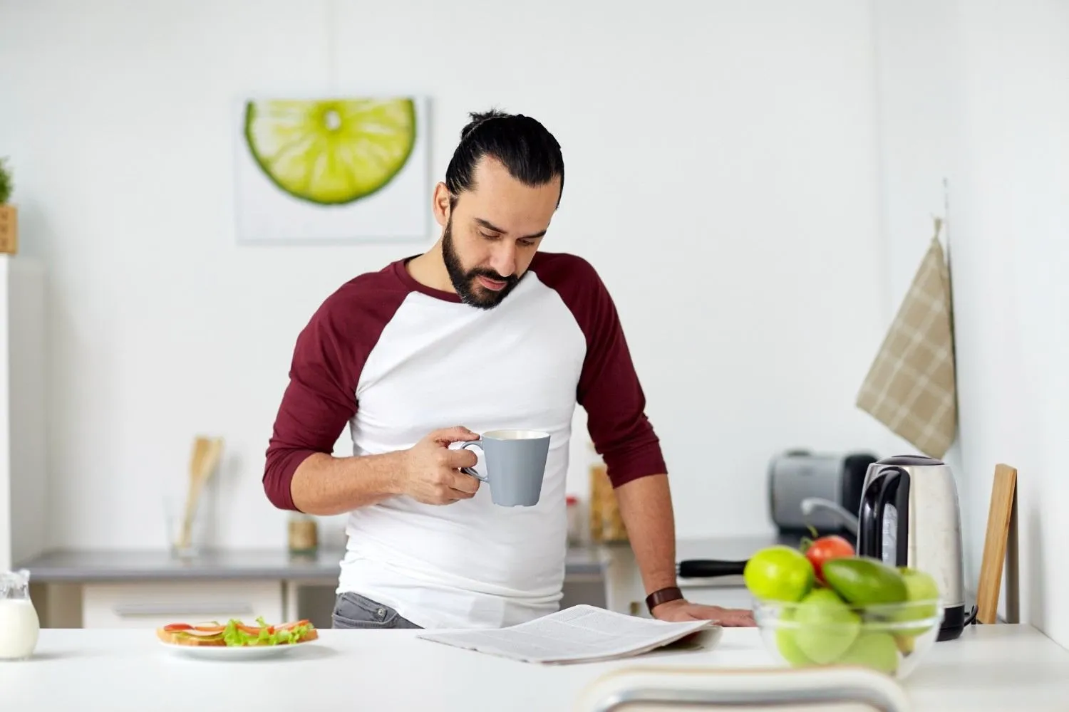 A man standing at a kitchen counter with a warm drink, fresh apples and a light breakfast